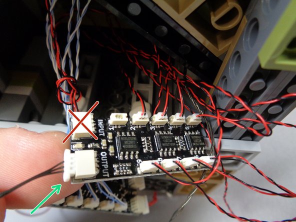 After you have connected all eight window lights to the BRANCH09X adapter board in the previous step, take the 24&quot; 3-black (or red) connecting cable you fed down into the castle base in Step 30 and connect it to the OUTPUT plug of the BRANCH09X adapter board, as shown by the green arrow in the first photo.