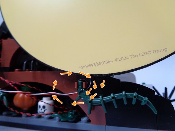 As shown in the second photo for this step, position the moon so the bottom notch and wire are aligned to the brown clip and green plant part.