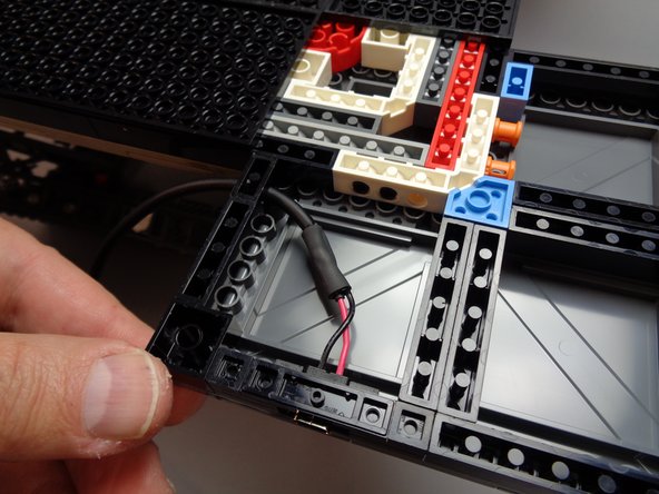 As shown by the green arrow in the first photo, take the black 1x4 brick provided with your Brickstuff kit and place it in the gap next to the power cable.