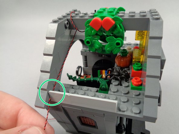 As shown by the green circle in the second photo for this step, carefully pull the LED light wire between the light bluish gray bracket and the rear roof frame.