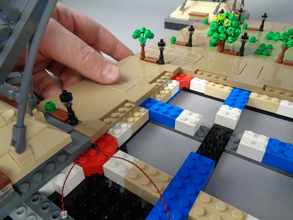 As shown in the third photo for this step, your LED light wires should pass between the studs on top of the red round brick and down into the open area by where your USB-C power wire is located.