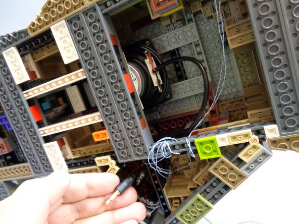 As shown in the first two photos, carefully insert the speaker facing upward into the space beneath the castle.  Gently press the speaker down so it sticks firmly to the two dark bluish gray plates as shown in the second photo.