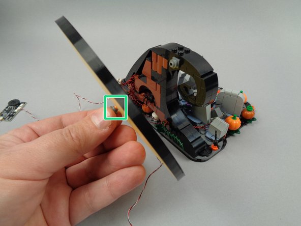 The green square in the first photo for this step shows the LEGO mounting pin re-inserted through the center of the paper moon.  Hold the moon by this pin and insert back into the round plate on the back side of the wave to re-attach the moon, frame, and LED strip.