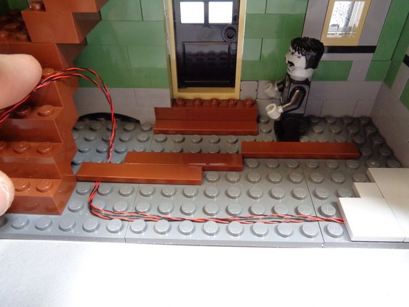 As shown in the first and second photos, replace the dark bluish gray plate and brown tiles you removed earlier.  These should now be holding the two fireplace light wires in place.