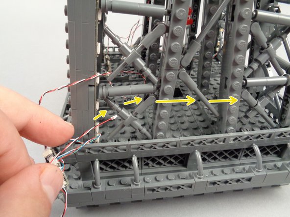 As shown by the yellow arrows in the second photo for this step, pass the other end of the control cable into the center of the top tower section and over toward the fourth and final pillar.