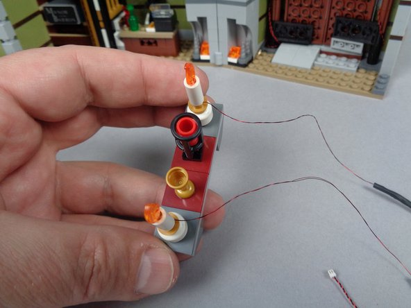 As shown in the second photo for this step, carefully press each candle down into the round gold LEGO plate on top of each skeleton head, making sure the light wire bends up through the top of the plate and out the back.