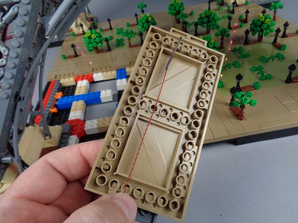 To prepare, bring the LED Light wire for the lamp post at the top of the panel underneath the panel as shown by the orange arrows in the first photo.  See the second photo for what the wire should look like once you have brought it under the panel.