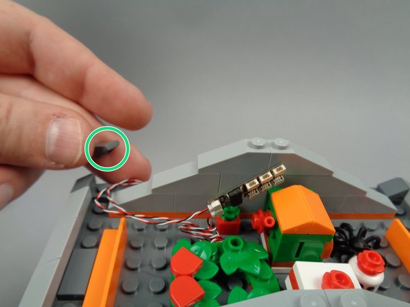 As shown by the green circle in the first photo for this step, remove the dark bluish gray 1x1 slope from the back of the town hall roof.