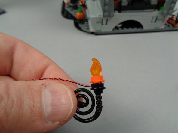 As shown in the two photos for this step, finish re-assembling the two torches by re-attaching the black whip pieces to the bottom of each.