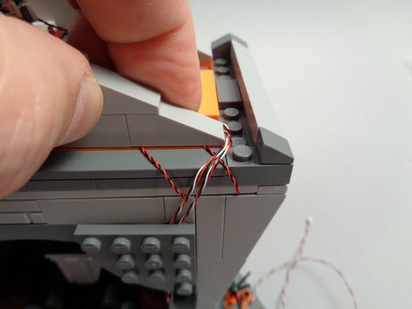 As shown in the photos for this step, now you can permanently mount the BRANCH06X driver board in the attic by re-attaching the 1x1 slope piece to hold the two control wires in place as shown in the second photo.
