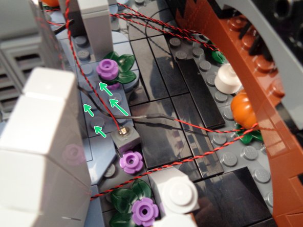 As shown in the first photo for this step, attach the third yellow LED Light to the base behind Zero's grave, positioned facing forward at an angle as shown by the green arrows.