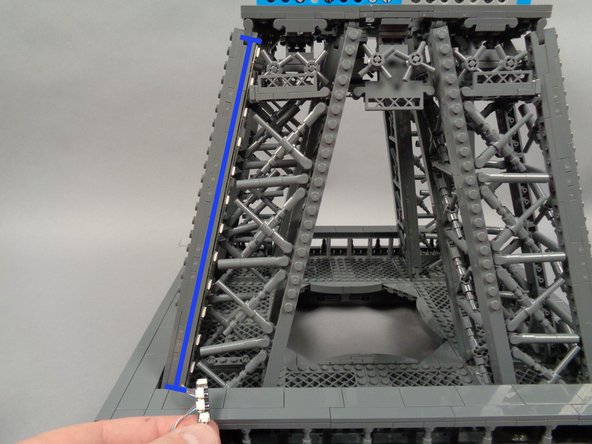 As shown in the second and third photos for this step, peel the backs off of the sticky squares on the first pair of light strips, and install the first strip, pressing with two fingers to make sure it adheres firmly to the tower frame.