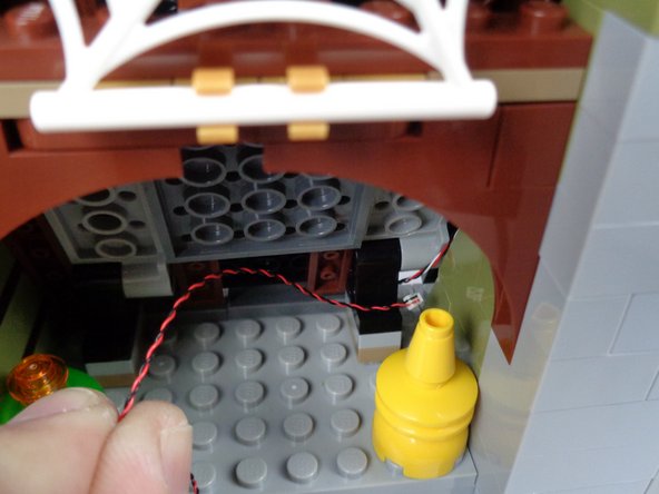 As shown in the first two photos for this step, pass the wire for the skull jar light toward the back of the attic and through the gap between the roof and floor.  Pull the wire out through the back of the mansion.