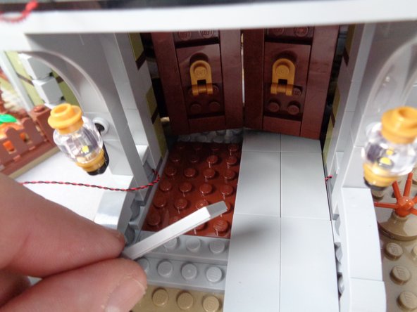 As shown by the green arrows in the third photo for this step, carefully run the light wire close to the wall toward the inside entryway of the mansion.