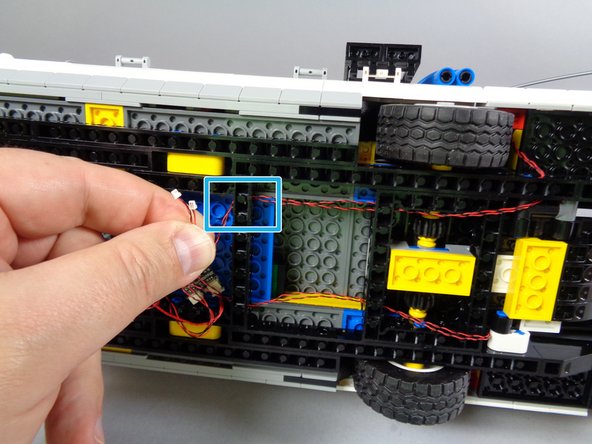 As shown by the blue rectangle in the second photo for this step, finish routing the two tail light wires by passing them through the hold in the Technic frame closest to the BRANCH09X adapter.