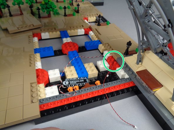 As shown by the green circle in the second photo for this step, route the two LED Light wires so they pass on top of the round red brick and back toward the BRANCH12X driver board.  Make sure wires pass between, not on top of, any studs.