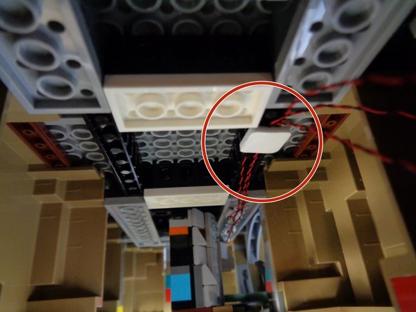 As shown by the red circles in the second and third photos, use one of the large sticky squares from Bag 1 to hold the three light wires to the top of the open space under the castle.