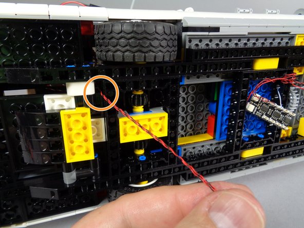Carefully turn your Ecto-1 on its side, and pull the two light wires down through the frame as shown by the orange circle.