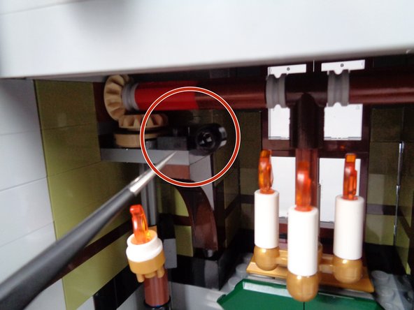 As shown in the second photo for this step, carefully place the plate above and to the left of the front door on the inside of the mansion, right next to the gears that open and close the front door.  See the red circle in the second photo.