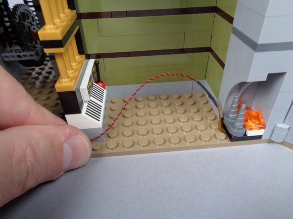 As shown in the second photo for this step, bend the fireplace light wire so it passes behind the desk area, then back toward the front of the elevator shaft.
