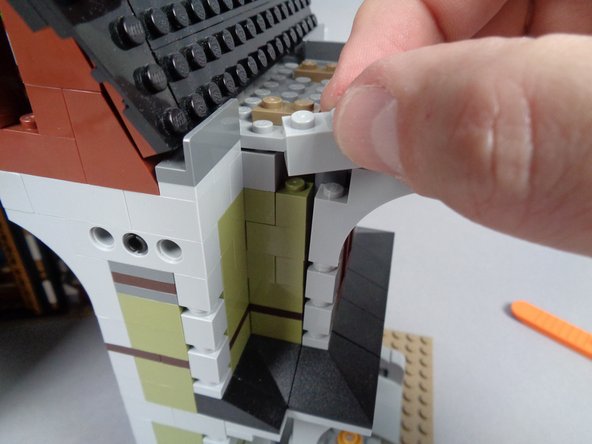 As shown in the two photos for this step, use the LEGO brick separator that came with your Haunted Mansion kit to pry up the baseplate above the window, then remove the 1x2 brick at the top of the wall.