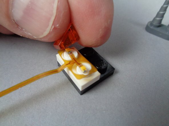 As shown in the first and second photos for this step, carefully re-attach the first LEGO flame slope piece by pressing it down over the top of the LED light from the flame assembly.