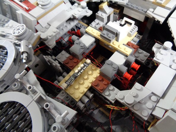 As shown by the dotted blue lines in the first photo of this step, run the red wire around the center of the Falcon so the BRANCH09 adapter board sits on top of the large tan plate in the center rear.