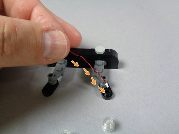 As shown by the orange arrows in the third photo for this step, pass the plug for the first light down through the hole in the black plate under the strobe.