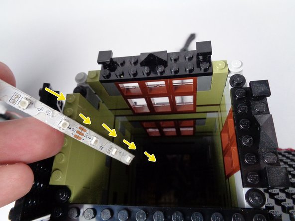 As shown by the yellow arrows in the second photo for this step, feed the light strip down toward the bottom of the elevator shaft on the side opposite the double windows.