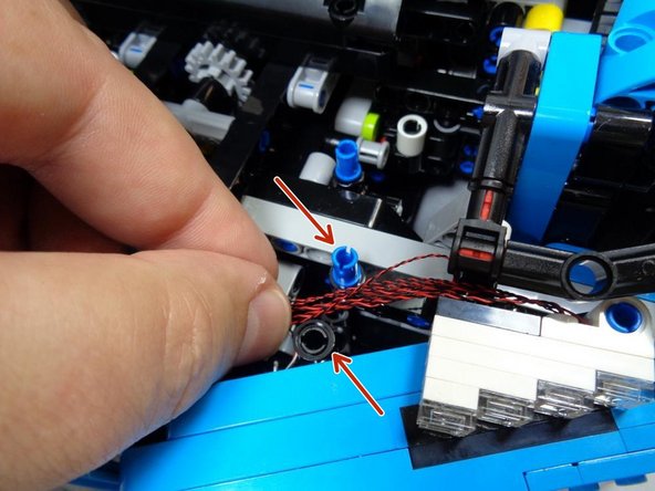 As shown in the second photo, carefully route the wires between the lower blue pin and the black beam (two red arrows in the second photo).