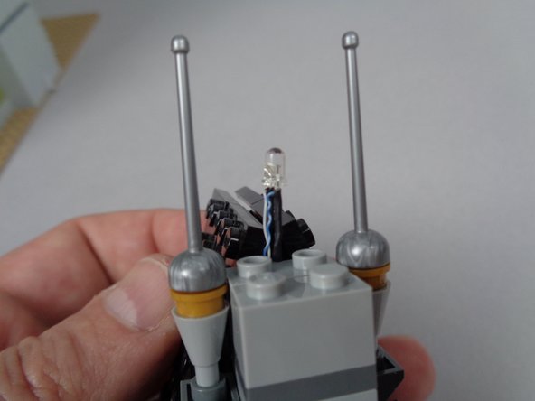 As shown in the first photo for this step, continue passing the LED light wire back through the hole at the top of the roof until the LED light is standing up right at the front of the gap.