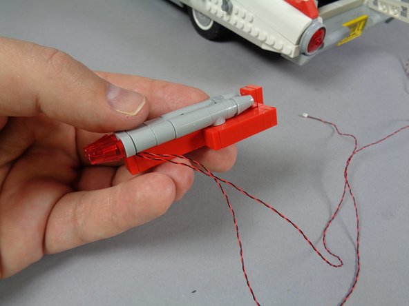 As shown in the photo for this step, re-assemble the left tail light section, and make sure the two LED light wires pass toward the right side.