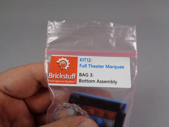 As shown in the first photo for this step, carefully remove the pre-lit replacement bottom marquee section from Bag 3.