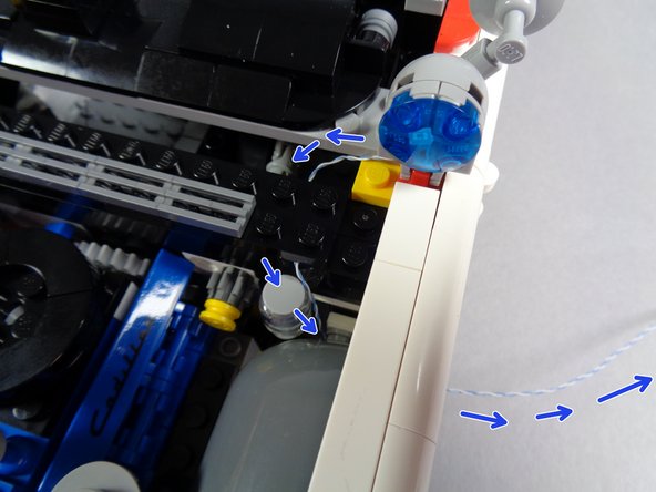 The blue arrows in the second photo for this step show how the wire should run down behind the wheel and out the side.