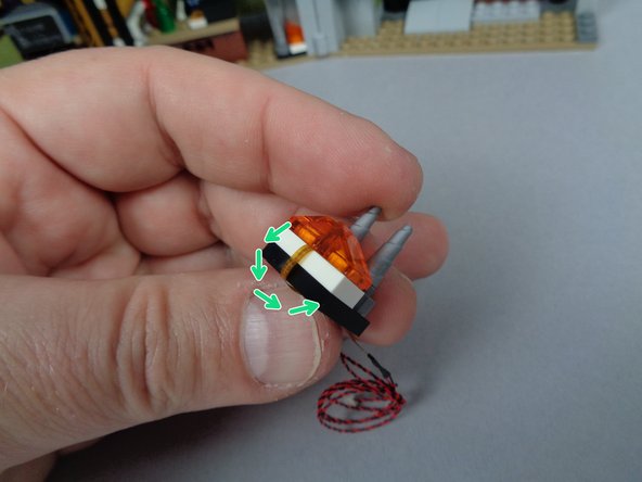 As shown by the green arrows in the second photo for this step, carefully bend the flexible wire back and underneath the 2x2 black LEGO plate that serves as the base for the fireplace.