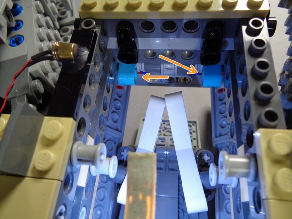 When you are finished, both arms and their Technic beams should look like the second photo.  Note the two orange arrows showing that both blue Technic pins have been removed.