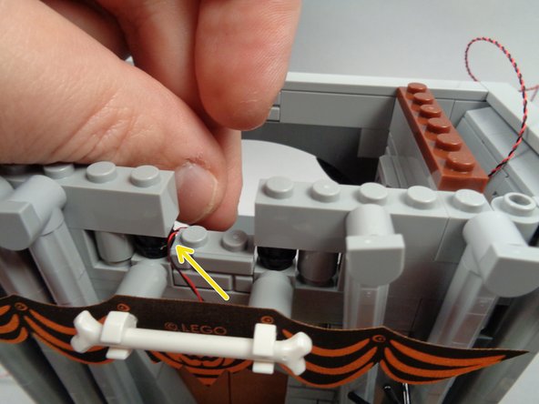 As shown by the yellow arrow in the second photo for this step, route the LED light wire to the side of the light bluish gray masonry pattern brick.