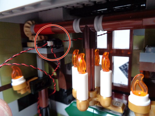 As shown by the red circle in the third photo, pass the plug for the front porch light wire through the hole in the black LEGO plate, right next to where the fireplace wire passes.