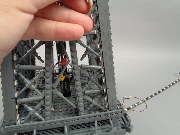 Remove the backs of the sticky dots on the first light strip (connected to plug #1 of the adapter board), and attach the strip to the tower frame as shown in the photos for this step.
