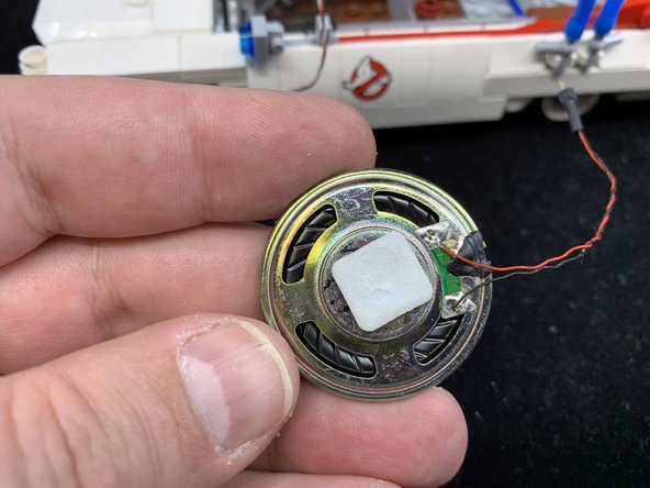 Attach one of the sticky squares included with your kit to the bottom of the speaker as shown in the first photo.