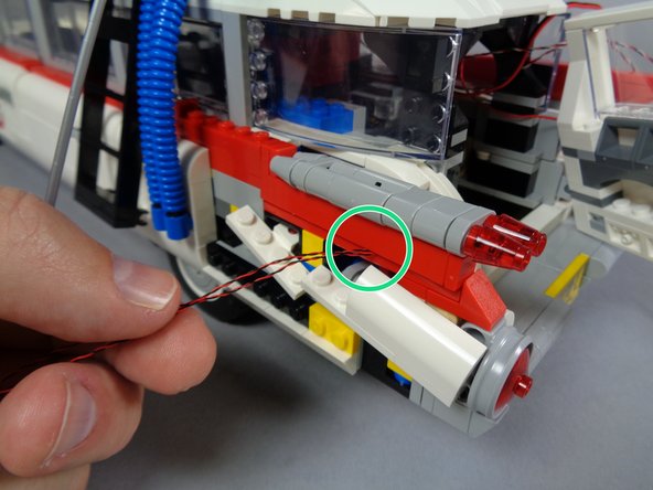 As shown by the purple arrows in the third photo, pass the two light wires along the vehicle frame (making sure they pass behind the white brackets), into the back of the vehicle, and then down underneath.