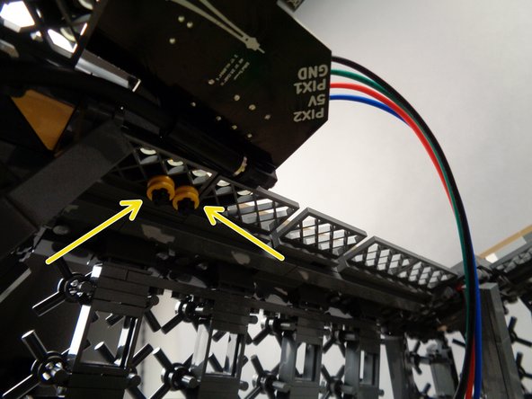 As shown by the yellow arrows in the first photo for this step, carefully press the remaining two round bushing pieces onto the bottom of the black axle parts.  Press down from the top while pressing up from the bottom to make sure the top and bottom bushings hold the board tightly in place.