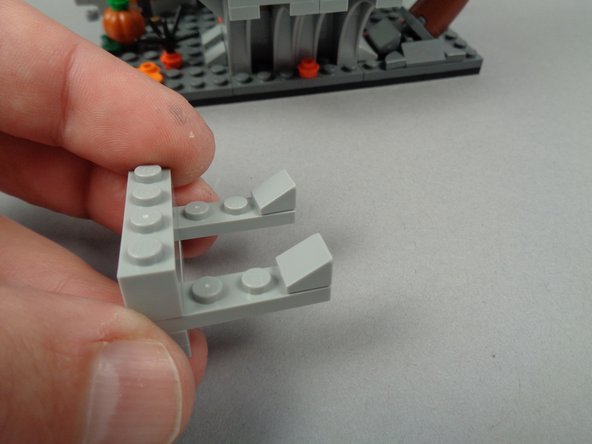 As shown in the second photo for this step, attach the two 1x1 slopes to the ends of the 1x4 plates of your wire support base.