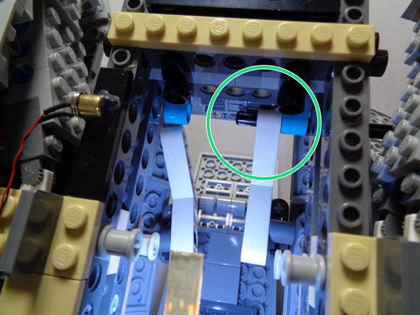 As shown by the red circle in the first photo, pass the black axle through the turquoise Technic beam.