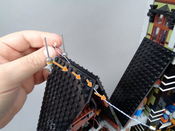 As shown by the orange arrows in the second photo for this step, carefully feed the plug end of the wire for the lightning LED light through the center of the roof and back towards the inside of the space above the organ.