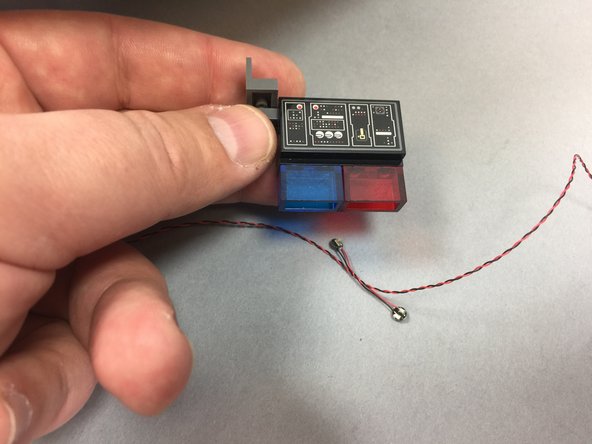 Inside the small bag labeled Interior Lights Parts, you will have one transparent blue 1x2 LEGO brick and one transparent red 1x2 brick.  Use those to replace the 1x4 black brick you removed in the previous step as shown in the first photo.