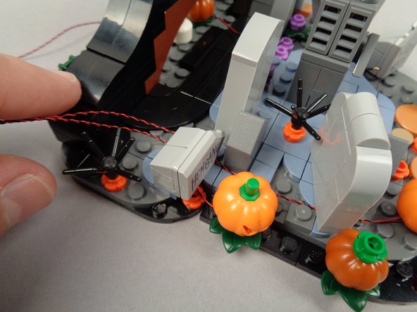 As shown in the third photo for this step, re-attach the HENBANE tombstone so it sits on top of the LED Light wires.