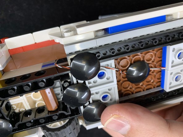 As shown in the second photo, on the underside of the car, remove the black &quot;boat stud&quot; on the right side, and hold the wire so it is BETWEEN the four studs shown by the four red circles in the photo.