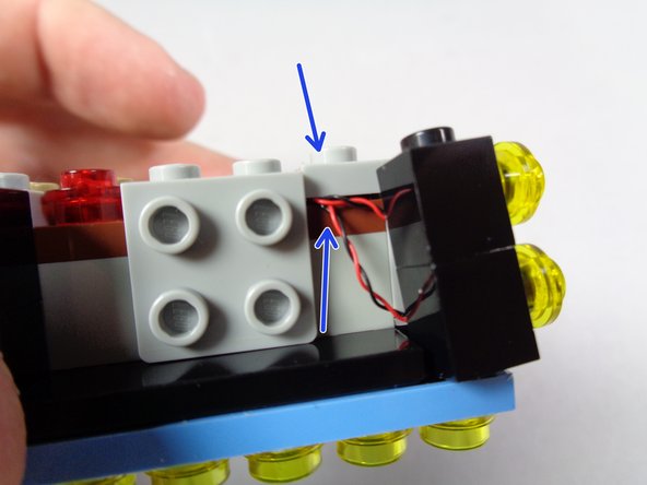 As shown by the orange rectangle in the second photo, carefully re-attach the gray bracket so the wires pass underneath.  The bracket should hold the wires, and the two black bricks, in place.