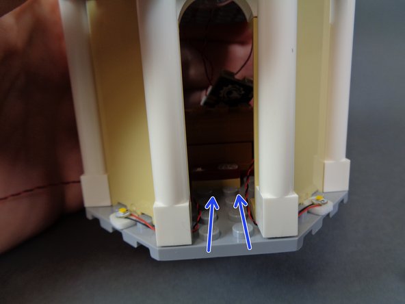 As shown by the two blue arrows in the first photo, route the wires from the two LED lights back into the interior of the tower.